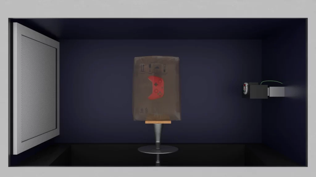 3D-CT-Scanner-Setup mit Gamecontroller in der Box Röntgenquelle rechts, Detektor links, mit einer Box dazwischen, in der ein roter Gamecontroller sichtbar ist.