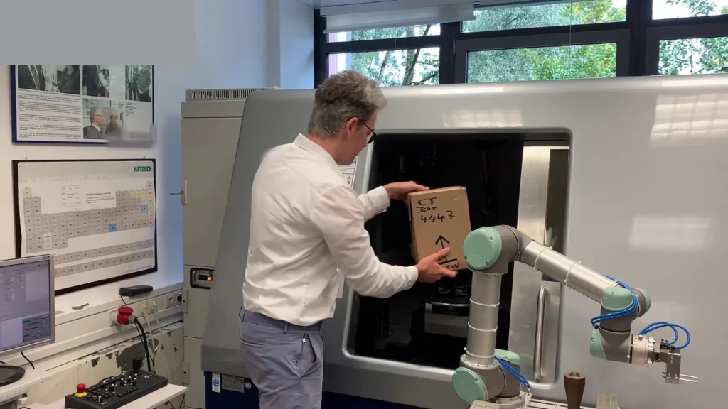 Box in den 3D-CT-Scanner stellen Mann platziert beschriftete Box in einen offenen 3D-CT-Scanner mit massiver Tür.